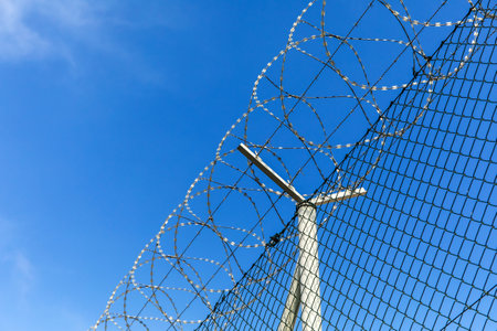 Barbed wire against a blue sky. Prison concept. Entry order. Military base. Detail of New Fence with...
