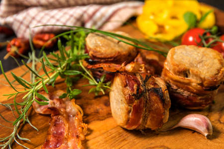 Grilled pork medallions with herbs and spices. Pork tenderloin with bacon. Grilled meat and tomatoes. Summer barbecue.の写真素材