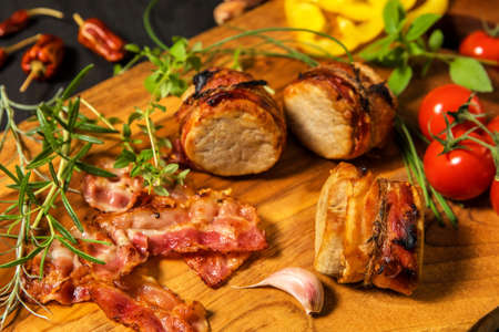Grilled pork medallions with herbs and spices. Pork tenderloin with bacon. Grilled meat and tomatoes. Summer barbecue.の写真素材