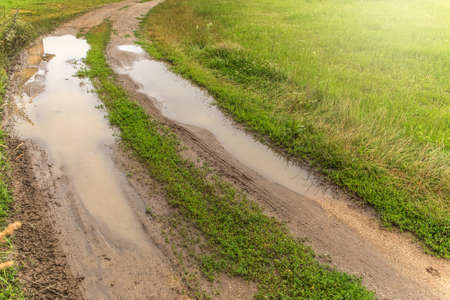 Big puddles on rut road after rain in summer. Muddy field road with a puddle in the Czech countryside. Water on the way.の写真素材
