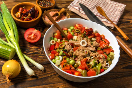 Tasty tuna salad with vegetables on wooden table. Vegetable salad with tuna. Preparing a healthy vegetable salad with fish. Diet food for athletes.の写真素材