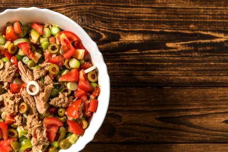 Tasty tuna salad with vegetables on wooden table. Vegetable salad with tuna. Preparing a healthy vegetable salad with fish. Diet food for athletes.の写真素材