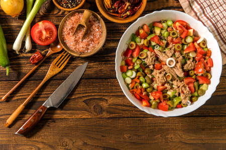 Tasty tuna salad with vegetables on wooden table. Vegetable salad with tuna. Preparing a healthy vegetable salad with fish. Diet food for athletes.の写真素材