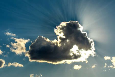 Sun is shining from behind the clouds. Blue sky with clouds and sunbeams. Sun hidden behind a cloud.の写真素材