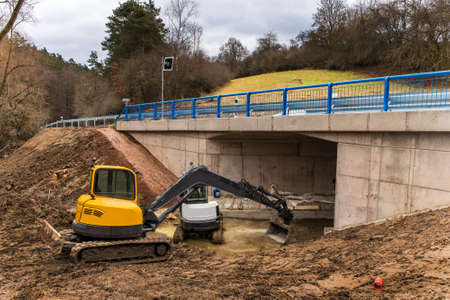 Excavator adjusts the terrain around the new bridge. Finishing work on the construction of a bridge...