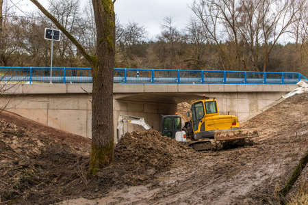 Excavator adjusts the terrain around the new bridge. Finishing work on the construction of a bridge on a country road in the Czech Republic.の写真素材