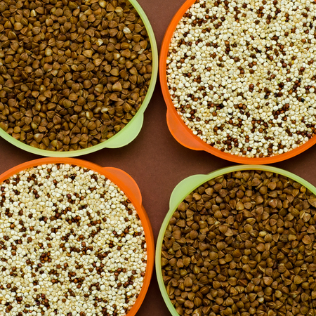 Four plastic containers with two kinds of grain. Two round plastic yellow containers with buckwheat and two round plastic containers with quinoa on the brown background.の写真素材