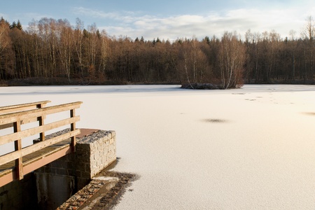 View of the winter landscape with a footbridge to the pond with an islandの写真素材