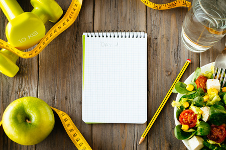 Workout and fitness dieting copy space diary  Healthy lifestyle concept  Salad, apple, dumbbell, water and measuring tape on rustic wooden table の写真素材