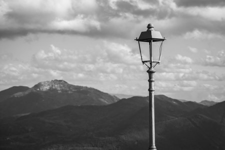 Black and white photo of a street lamp against the background of the mountainsの写真素材