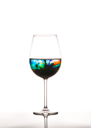 Glass with multicolored water on white background, concept of polutionの写真素材