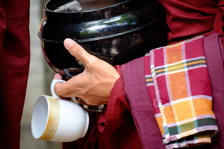 Detail of buddhist monk in red robe, his hands holding a bowl and cupの写真素材