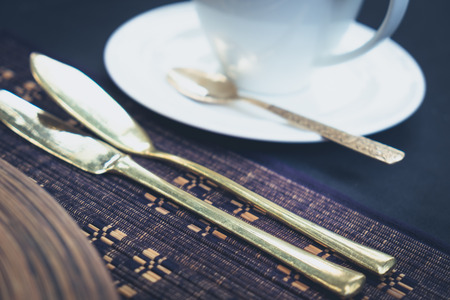 Nice detail of golden cutlery and a cup laid on a table
