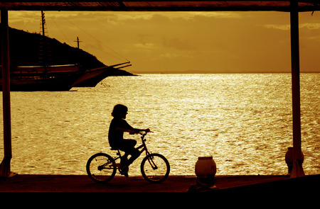 Boy on bike over harbor at sunsetの写真素材