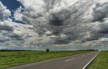 road is lost in the horizon with cloudy sky and green fieldsの写真素材