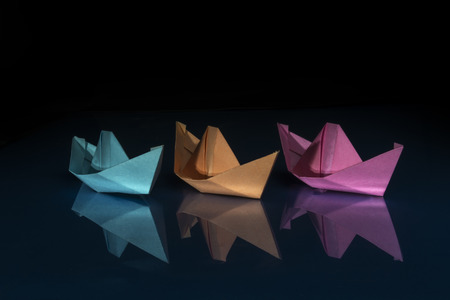 three ships of different colored paper on blue and black background