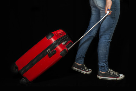young girl with jeans and sneakers hauling a red suitcase, all over black backgroundの写真素材