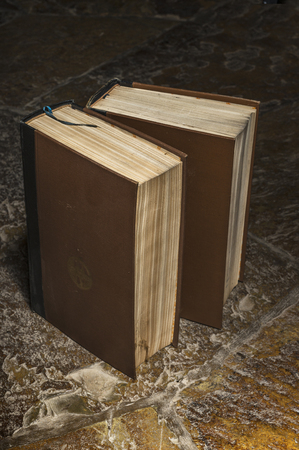 two old brown books standing on a stone floorの写真素材