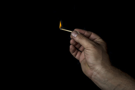Man's hand holding a match on black backgroundの写真素材