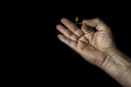 Man's hand holding a match on black backgroundの写真素材