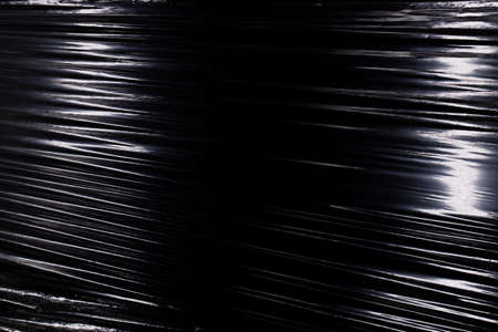 Glare on stretched wrinkled cling film, texture of plastic packaging on a black backgroundの写真素材