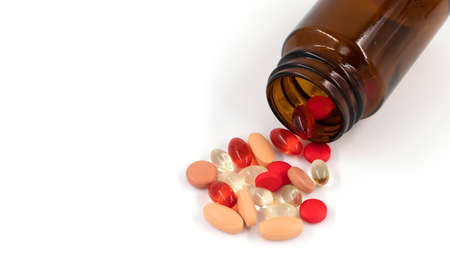 Multicolored pills and pills spilling from amber glass bottle isolated on white, medicine concept...