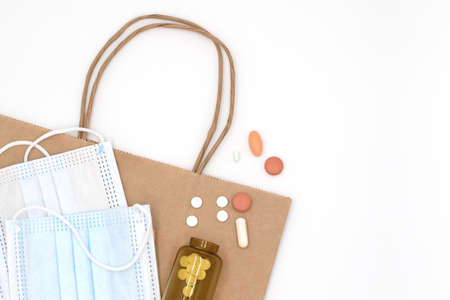 Sterile masks, pills and medication capsules spilled from amber glass bottle on white background,...