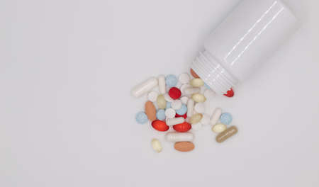 Heap of multi-colored pills and capsules, medicines scattered from a sterile container on white...