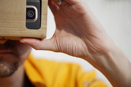 Male hands holding a cardboard goggles on the face as a symbol of modern digital life and symbol of a  tool used for watching movies and playing games in virtual realityの写真素材