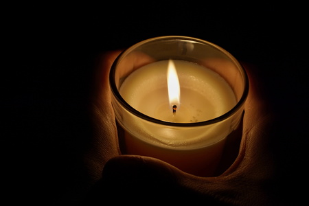 Male hands holding a candle in the transparent glass shining in the darkness as a symbol of...