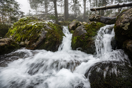 rocky waterfall in winter with stream and high water in forestの写真素材