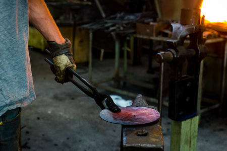 The blacksmith manually forging the molten metal on the anvil in smithy with spark fireworksの写真素材