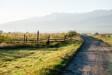 Winding country Road with clouds above and gravel surface and wooden fenceの写真素材