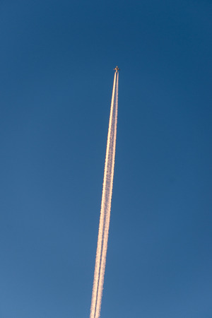 The plane flies low in the sky, leaving a white trail.の写真素材