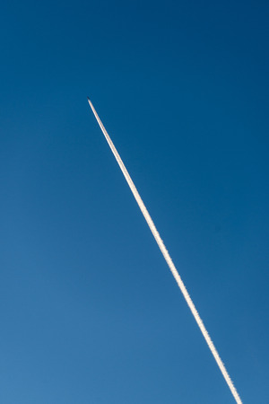 The plane flies low in the sky, leaving a white trail.の写真素材