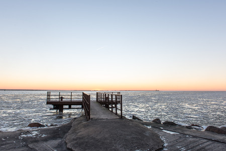 sunset over frozen sea with ice blocks and dramatic colorful sky with old metal bridgeの写真素材