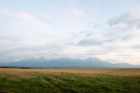 Dark storm clouds over meadow with green grass and mountains in backgroundの写真素材
