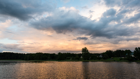 Beautiful summer sunset at the river with blue sky, red and orange clouds, green trees and water with reflectionの写真素材