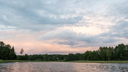 Beautiful summer sunset at the river with blue sky, red and orange clouds, green trees and water with reflectionの写真素材