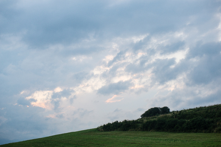 Dark storm clouds over meadow with green grass and mountains in backgroundの写真素材