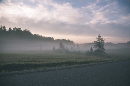 misty countryside landscape in latvia with asphalt wavy road in autumn. cold morning - vintage lookの写真素材