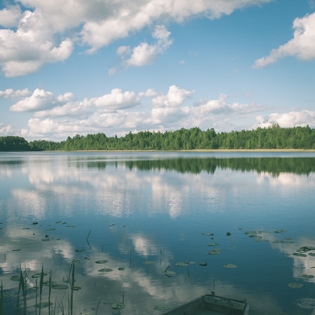 White clouds on the blue sky over blue lake with reflections with boats and boardwalk - instant vintage square photoの写真素材
