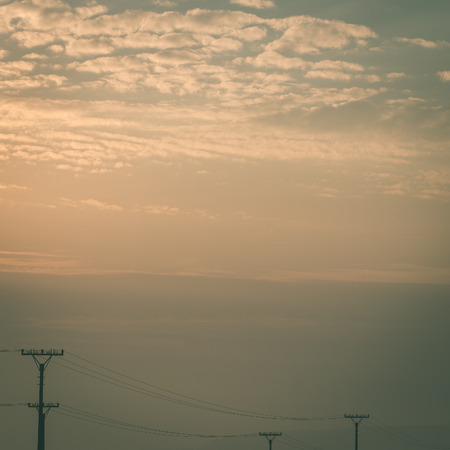 sunset over the fields in fog in summer with electricity poles - instant vintage square photoの写真素材