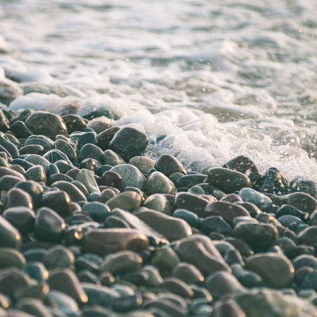 sun reflections on Stones on the beach and sea water in sunset light - instant vintage square photoの写真素材