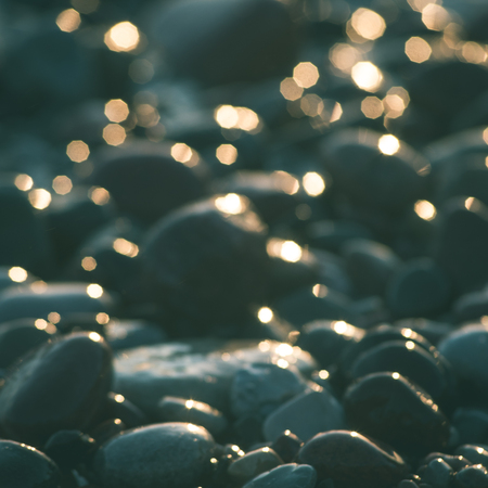 sun reflections on Stones on the beach and sea water in sunset light - instant vintage square photoの写真素材