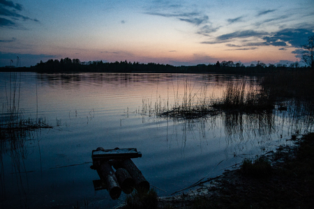 sunset over the calm lake beach with dramatic colorful sky and tree silhouettesの写真素材