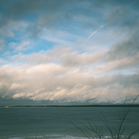 moody overcast winter day at the lake with rain and raindrops, dramatic sky - instant vintage square photoの写真素材