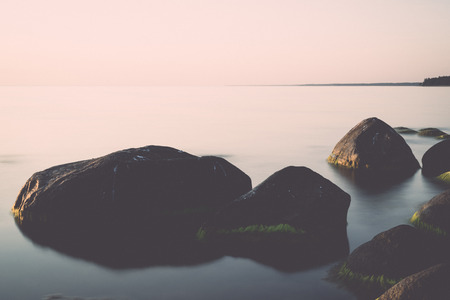rocky beach at sunset with milky water - retro, vintage style lookの写真素材