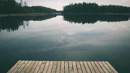 reflection of clouds in the lake with nice wooden boardwalk and trees in background - vintage green lookの写真素材