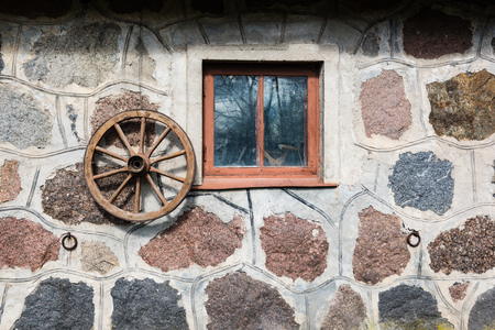 old rock building in latvia countryside with window and wooden wheelの写真素材